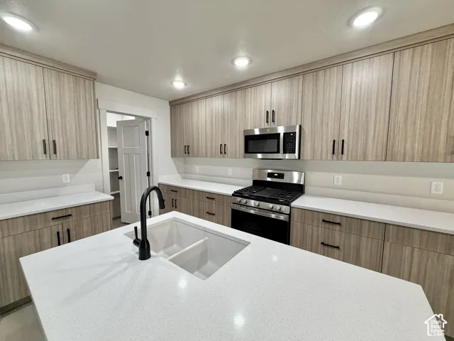 Kitchen featuring flat-panel wood-grain cabinetry, quartz countertops, a central island with an undermount dual-basin sink, matte black hardware, and stainless steel appliances