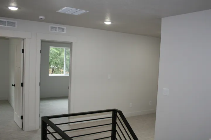 Interior hallway with neutral tone walls, recessed lighting, and a modern metal stair railing