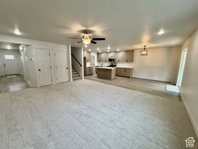 Open-concept interior featuring light wood-finish cabinetry, a central kitchen island, recessed lighting, neutral carpeting, and wood-finish flooring