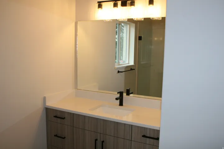 Wood-finish vanity with ample storage, white solid surface countertop, integrated rectangular sink, matte black single-handle faucet, and rectangular mirror
