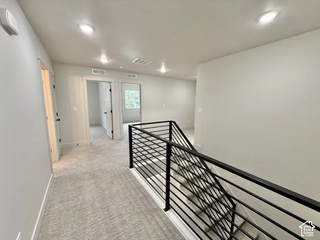 Neutral wall tones, carpeted flooring, recessed ceiling lighting, and a black metal horizontal-bar staircase railing