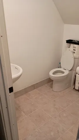 White wall-mounted sink, white two-piece toilet, and neutral-toned tile flooring