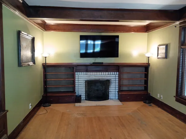 Built-in shelving flanking a brick fireplace, wood-finish flooring, and wood beam ceiling