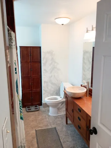 Bathroom featuring a wood-finish vanity with vessel sink, wall-mounted mirror, overhead lighting, and tiled flooring