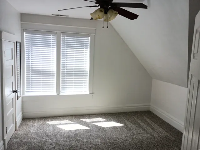 Window with white blinds, wall-mounted ceiling fan, angled ceiling, white trim, and carpeted flooring