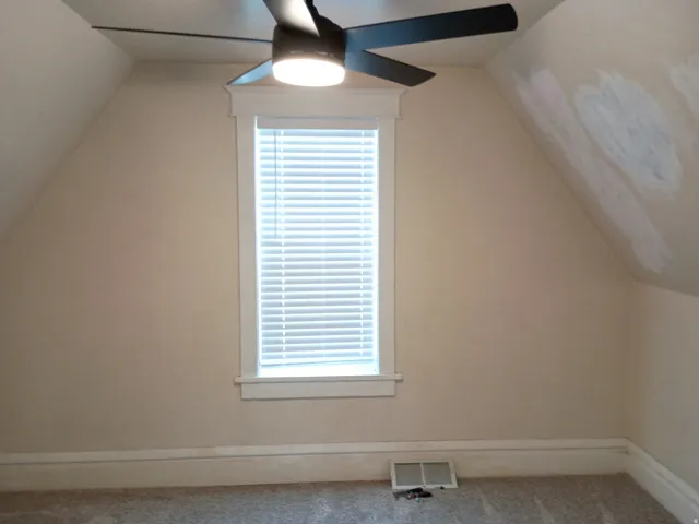Sloped ceiling design with a ceiling fan, a window with blinds, and neutral-toned carpeting