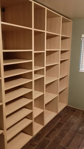 Built-in shelving with adjustable shelves, light wood-finish cabinetry, and dark wood-look flooring