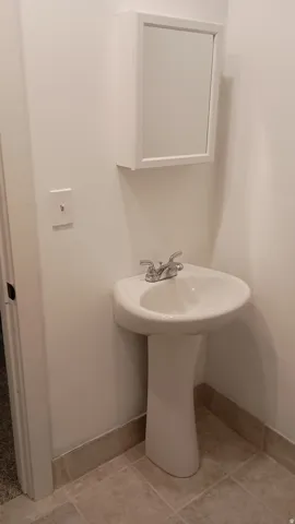 Pedestal sink with a two-handle faucet, wall-mounted medicine cabinet, and tiled flooring