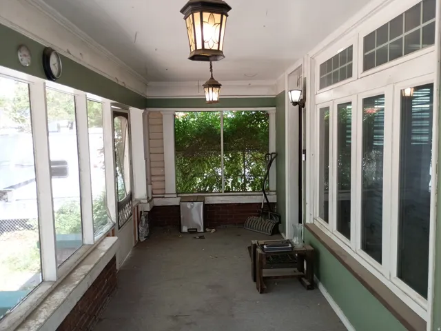 Enclosed porch featuring multiple window panels, two hanging light fixtures, crown molding, and painted brick accents