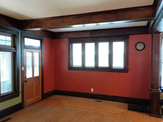 Wood-finish flooring with a herringbone pattern, exposed ceiling beams, and a wood-paneled door with frosted glass inserts