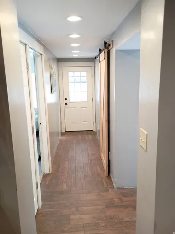 Recessed ceiling lighting, wood-finish flooring, paneled interior door with glass inserts, and a sliding barn door