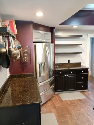Stainless steel refrigerator with a water/ice dispenser, dark wood-finish flooring, dark cabinetry with white knob hardware, and brown speckled countertops