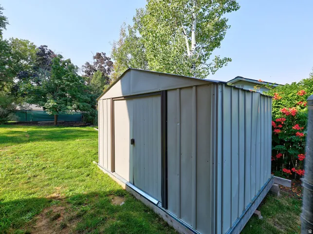 Metal storage shed with a sliding door, positioned on a grassy area