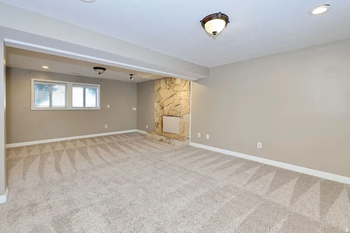 Spacious room featuring neutral carpeting, a stone-clad fireplace with a hearth, multiple windows, and recessed lighting