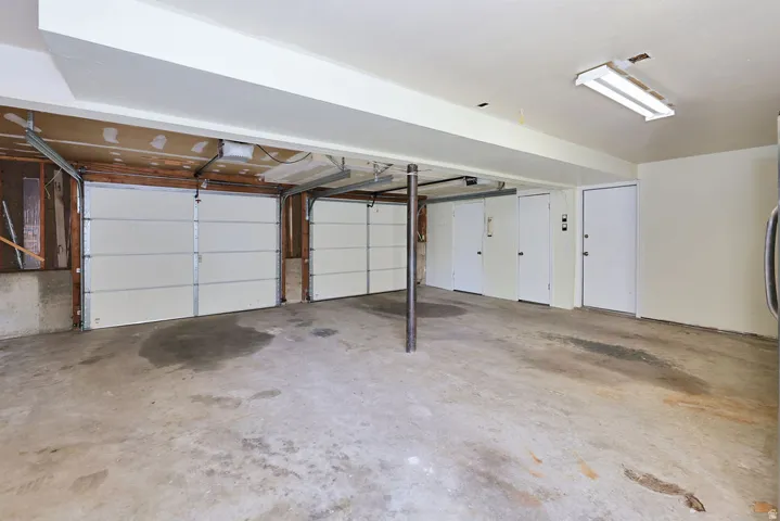 Two overhead garage doors, concrete flooring, exposed ceiling beams, built-in fluorescent lighting