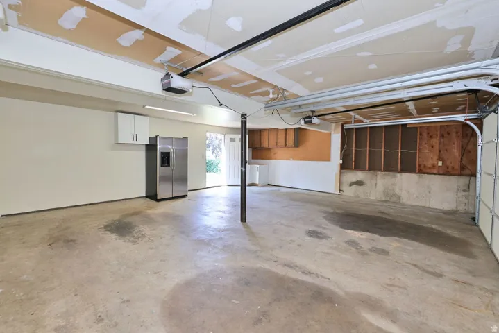 Attached garage with concrete flooring, overhead lighting, and white cabinetry