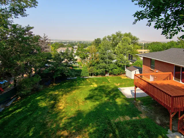 Expansive backyard with a manicured lawn, established trees, and a spacious wood deck