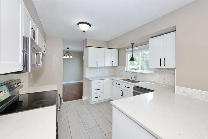 Kitchen featuring white shaker cabinetry, stainless steel appliances, light-toned countertops, and a full tile backsplash