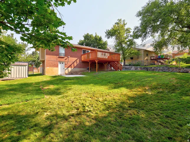 Expansive backyard featuring a manicured lawn, a detached storage shed, a ground-level patio, and a raised wood deck with staircase access