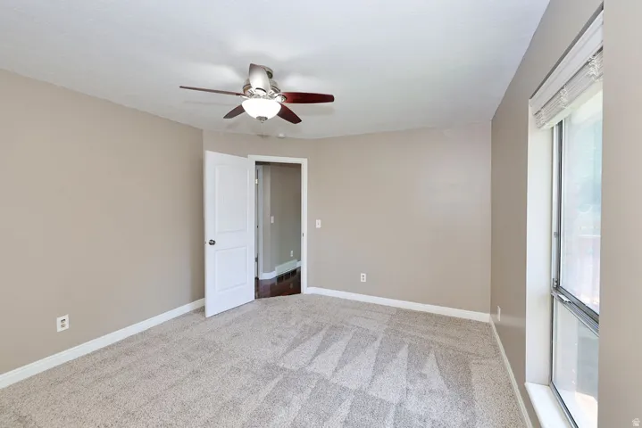 Neutral wall tones, patterned carpeting, ceiling fan with integrated lighting, and a window with blinds
