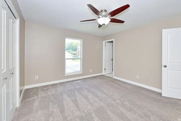 Carpeted room with a ceiling fan, a window, and two paneled doors