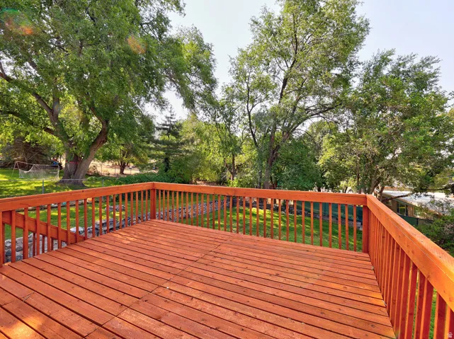 Expansive wooden deck with a finished surface and railing, overlooking a lush green lawn and mature trees