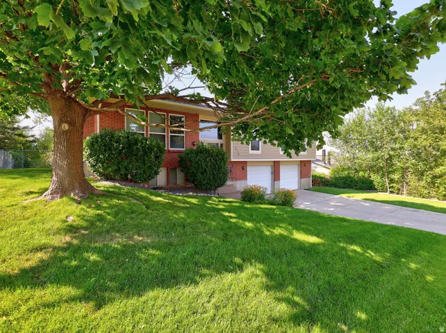 Brick and siding exterior with a lush lawn, established trees, and an attached two-car garage
