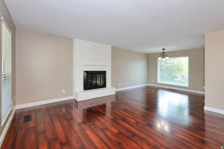 Expansive room with wood-finish flooring, a white brick fireplace, a large window, and a chandelier