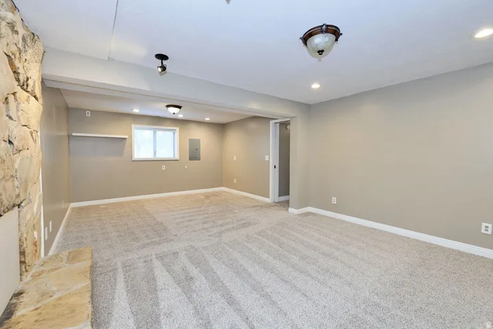 Spacious room with plush carpet, stone-faced wall, recessed lighting, and a double-pane window