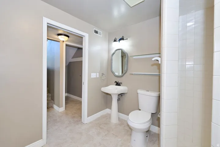 Pedestal sink, ceramic tile flooring, enclosed shower, wall-mounted light fixture, and framed mirror