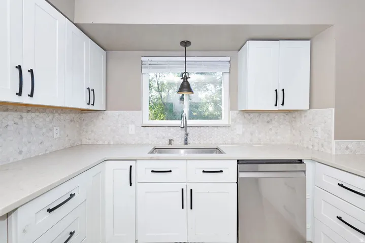 White shaker-style cabinetry, light-toned countertops, mosaic tile backsplash, stainless steel sink, and stainless steel dishwasher