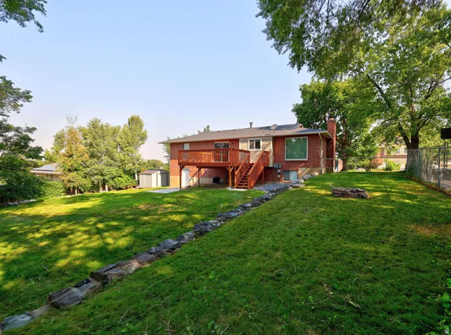 Expansive backyard featuring a lush lawn, mature trees, a multi-level wood deck, and a brick exterior