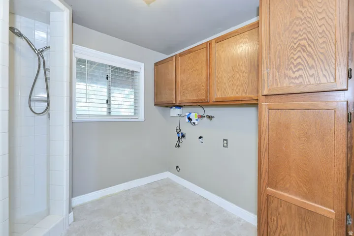 Shower enclosure with white tile, wood-finish cabinetry, window with blinds, and neutral wall paint