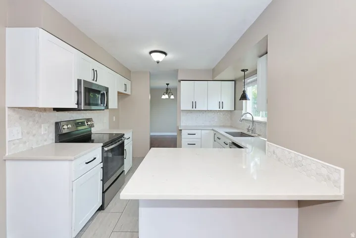 White shaker cabinetry with dark hardware, stainless steel appliances, light-colored countertops, tile flooring, and a tiled backsplash
