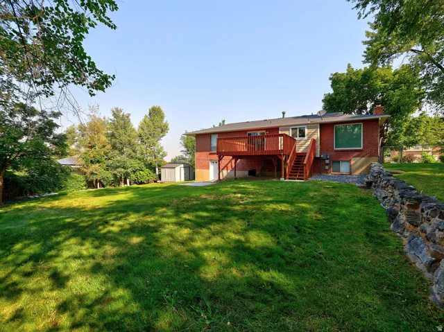 Expansive grassy yard with a stone retaining wall, large wood deck, and a detached shed