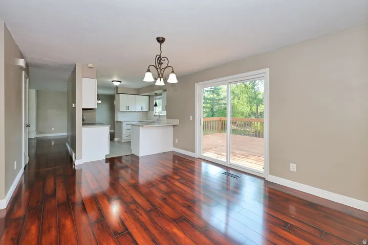 Wood-finish flooring throughout, with a decorative chandelier, and white kitchen cabinetry