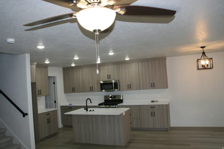Modern kitchen featuring extensive cabinetry, stainless steel appliances, a center island with sink, recessed lighting, and wood-finish flooring