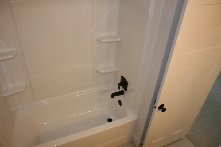 White acrylic tub and shower combination with integrated shelving and matte black fixtures
