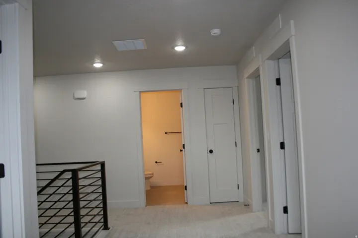 Carpeted hallway featuring a black metal railing, recessed lighting, and white paneled doors with black hardware