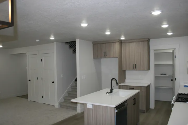 Kitchen island with an undermount sink and matte black faucet, light wood-finish cabinetry, built-in shelving, stainless steel appliances, and recessed lighting