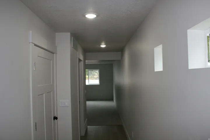 Recessed ceiling lighting illuminates a corridor featuring white walls and a white paneled door with black hardware