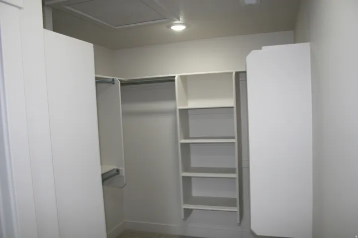Built-in white shelving, integrated hanging rods, recessed lighting, and a neutral color palette
