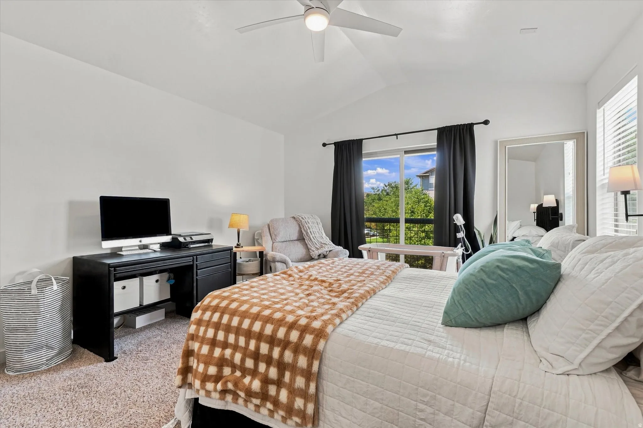 Vaulted ceiling, ceiling fan, large window with outdoor visibility, window blinds, and carpeted flooring