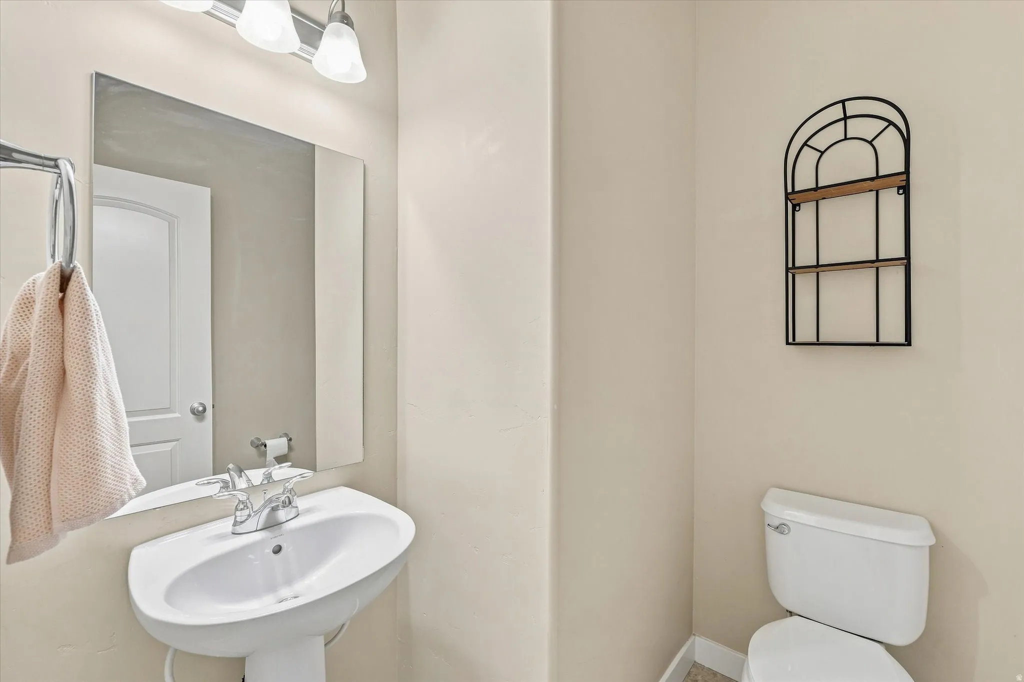 Pedestal sink with chrome faucet, wall-mounted mirror, and overhead vanity lighting