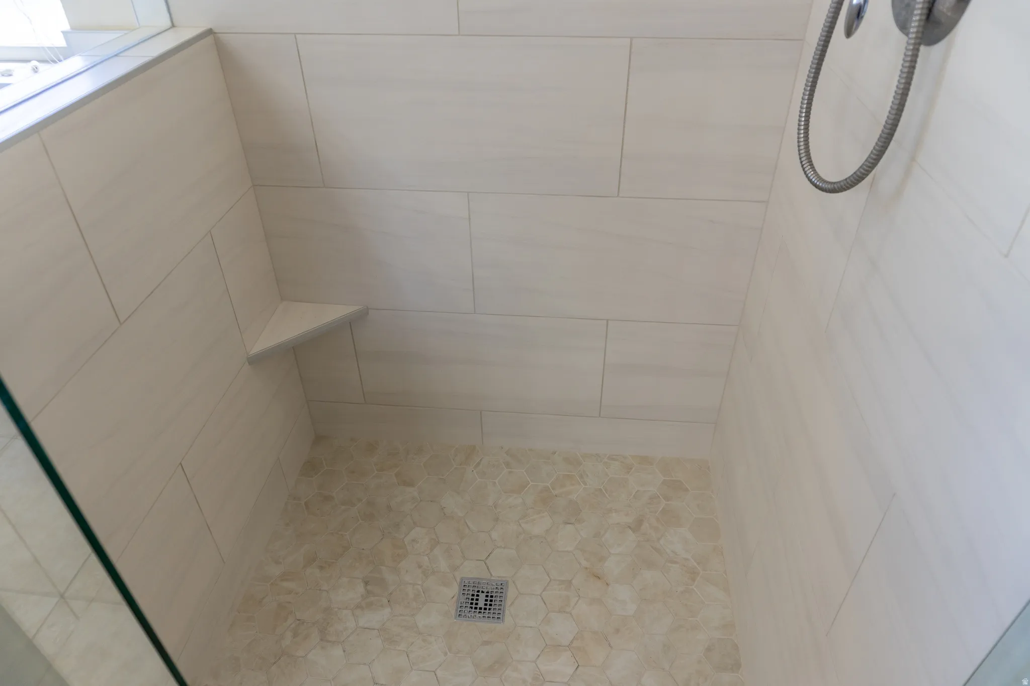 Tiled shower with a corner shelf, hexagonal floor tiles, and a glass enclosure