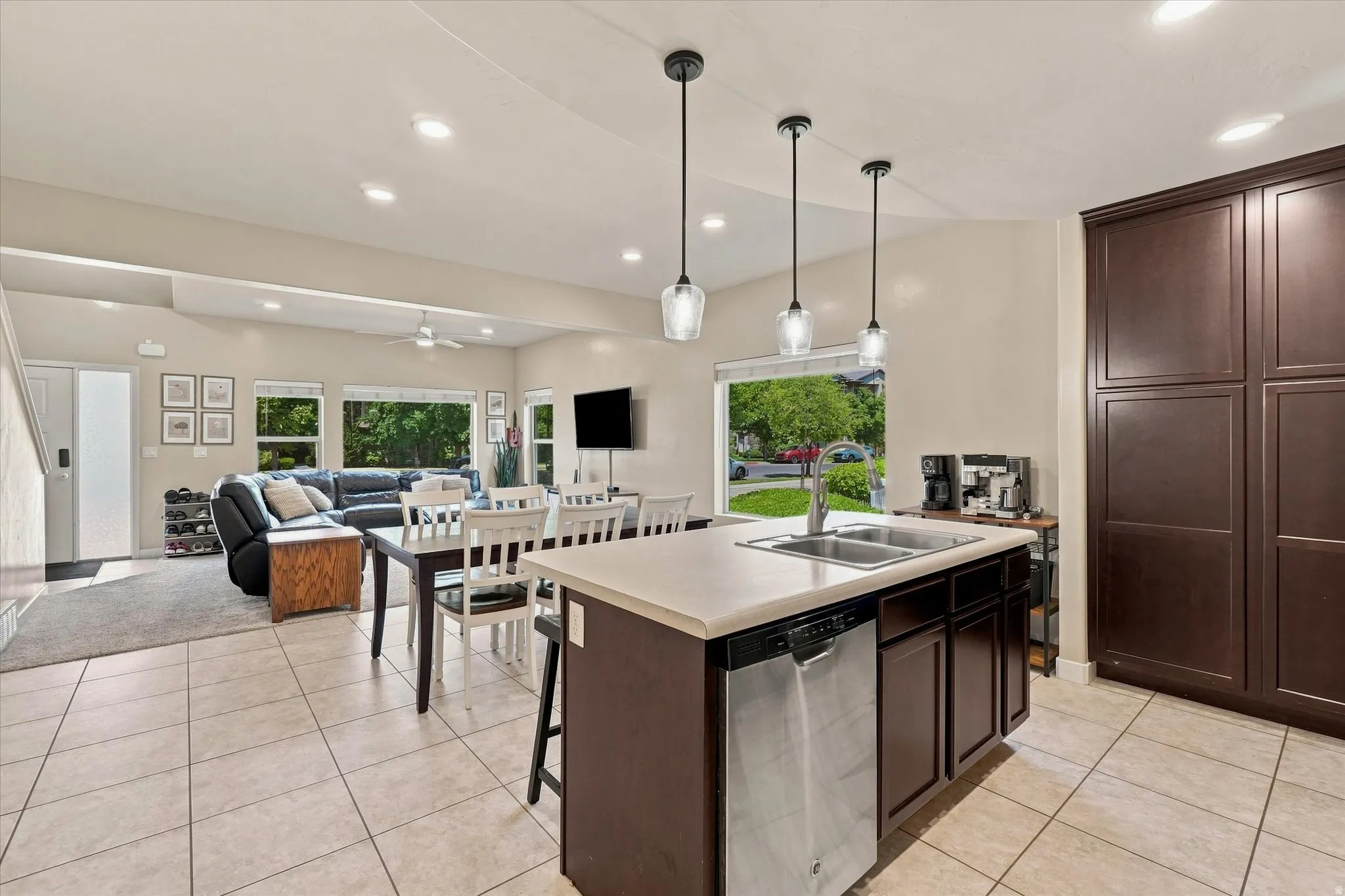 Kitchen island with a double basin sink and integrated dishwasher, dark wood-finish cabinetry, and tiled flooring