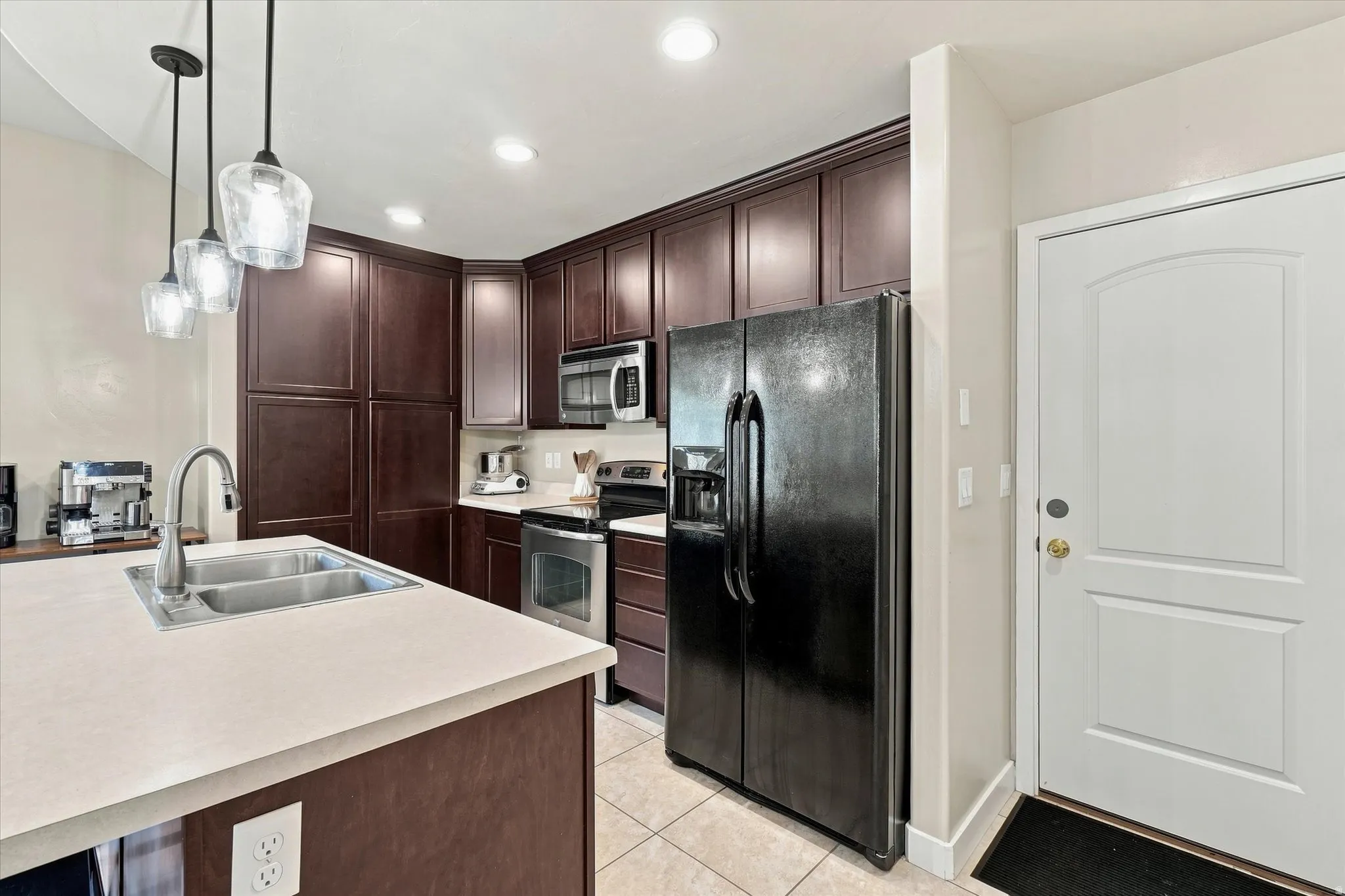 Kitchen featuring dark wood-finish cabinetry, stainless steel appliances, a double basin sink, and pendant lighting