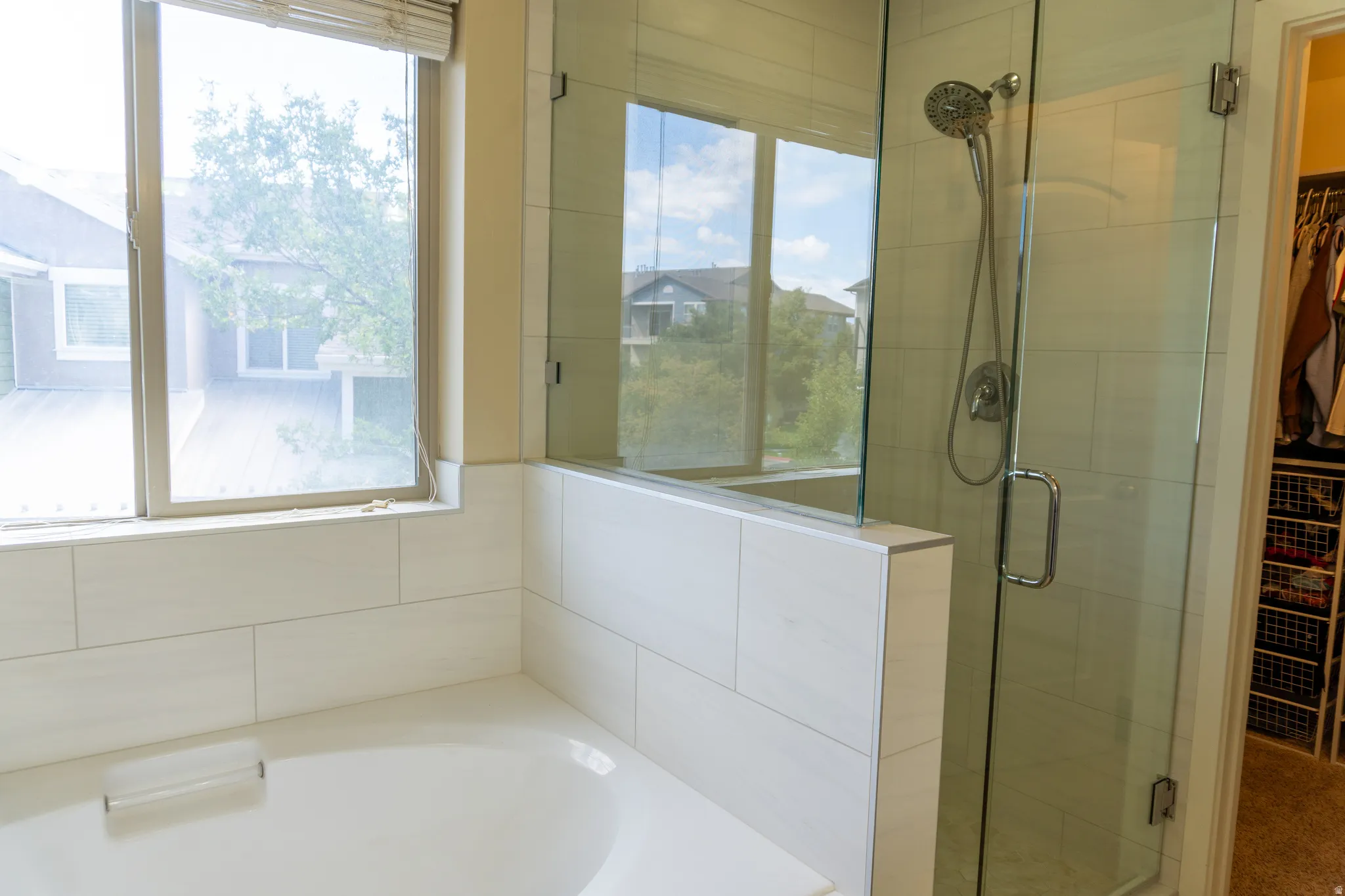 Built-in bathtub, tiled surround, window with blinds, glass-enclosed shower, and a chrome showerhead
