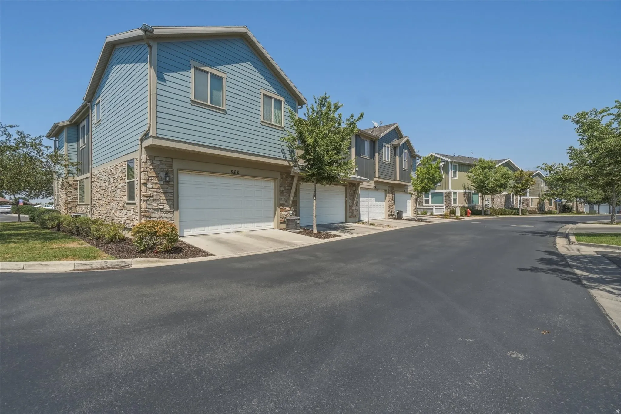 Exterior featuring stone and siding facade, attached two-car garage, and landscaped front yard with mature trees