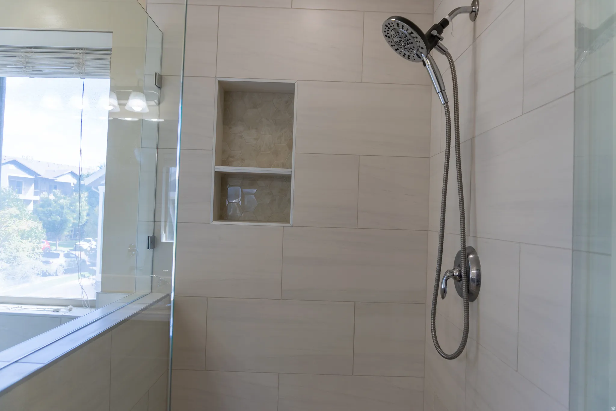 Tiled shower surround with a built-in niche, featuring a multi-function showerhead with a handheld sprayer, and glass enclosure
